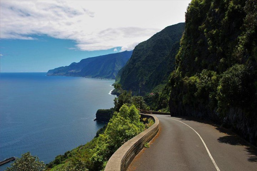 A winding coastal road with a view of the ocean and green hills. 1