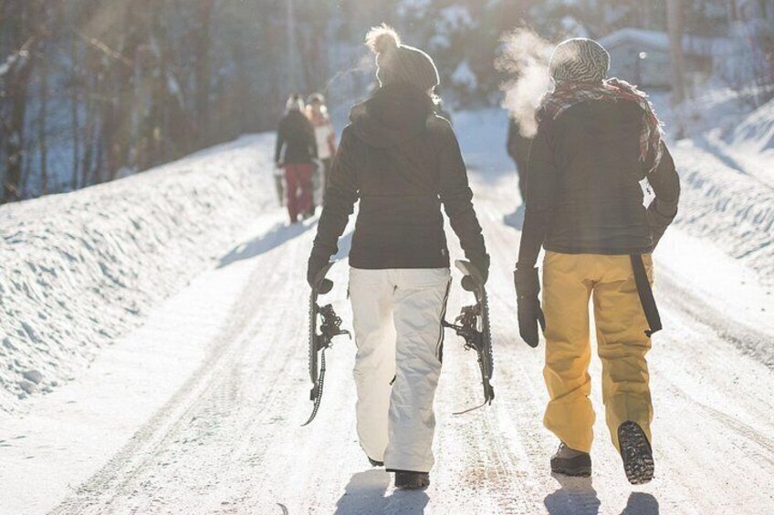 Two people walking on a snowy road with snowshoes, surrounded by trees. 3