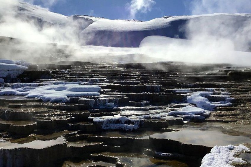 A geothermal area with steam rising from hot springs, snow-covered terrain, and ice formations. 4
