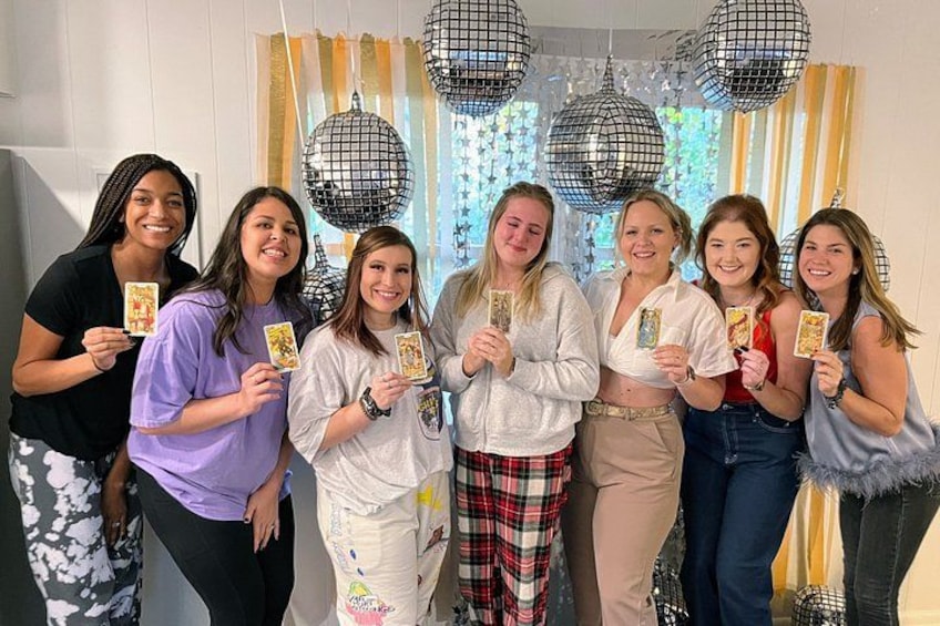 A group of people holding playing cards in a room with disco balls and striped curtains. 2