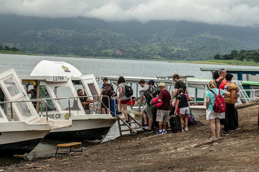Een groep mensen stapt aan boord van een boot, met een meer en bergen op de achtergrond. 4