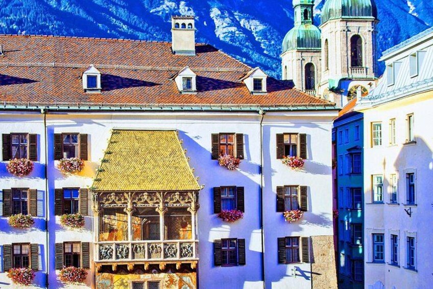 A European town with white buildings, a balcony with a wooden railing, and a church with a green dome. 1