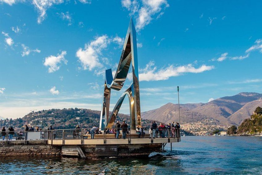 A waterfront sculpture, a pier, and a distant cityscape. 1