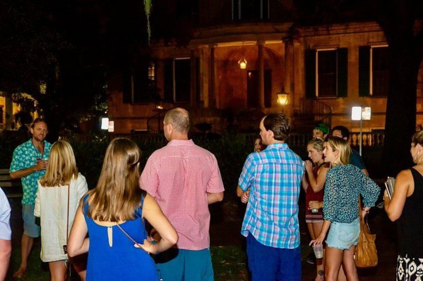 Een groep mensen die 's nachts buiten in een binnentuin met een gebouw op de achtergrond in gesprek zijn. 2