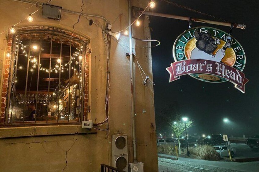 Un edificio con un letrero que dice 'Boar's Head Grill & Tavern' y una ventana decorada con luces de cadena. 2