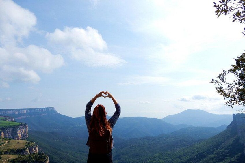 A person making a heart shape with their arms against a backdrop of a mountainous landscape. 4