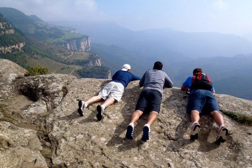 Three people resting on a rocky outcrop with a mountainous landscape in the background. 1