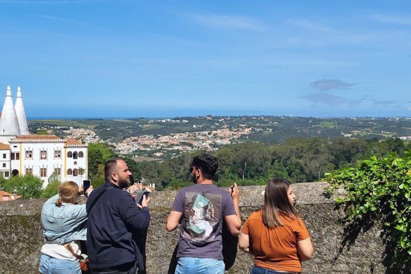 A group of people taking photos of a coastal town with a prominent church and a hilltop view. 5