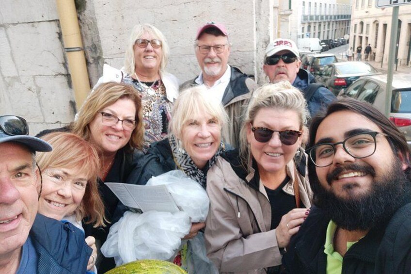 Un grupo de personas de pie al aire libre, algunas sosteniendo objetos, con edificios y coches aparcados al fondo. 2