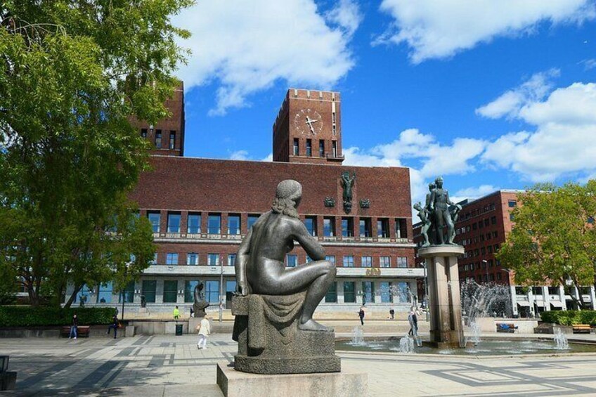 A sculpture of a seated figure, a clock tower, and a fountain in a public square. 3