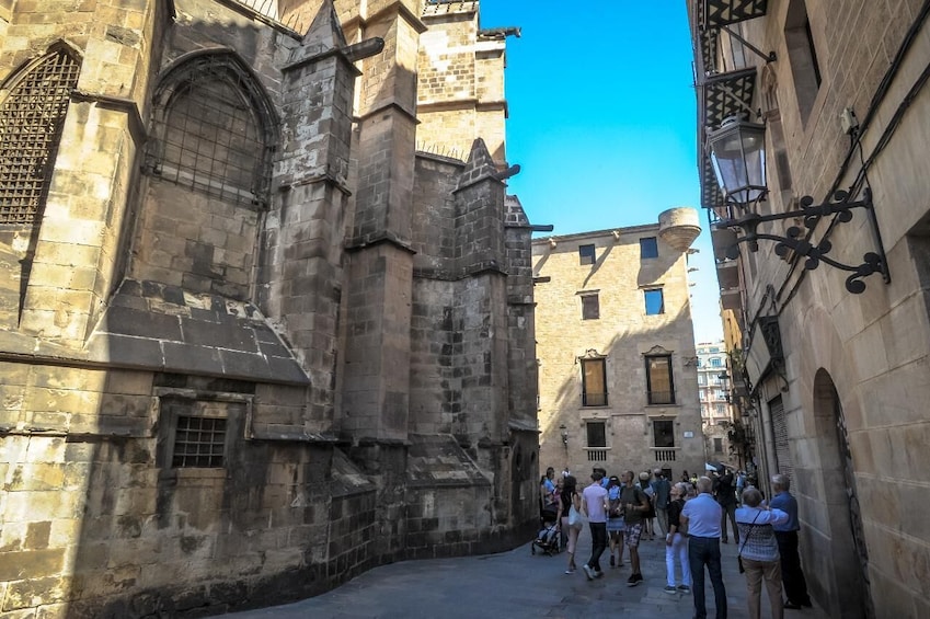 Una estrecha calle bordeada por edificios históricos de piedra con ventanas de arco y un cielo azul despejado. 4