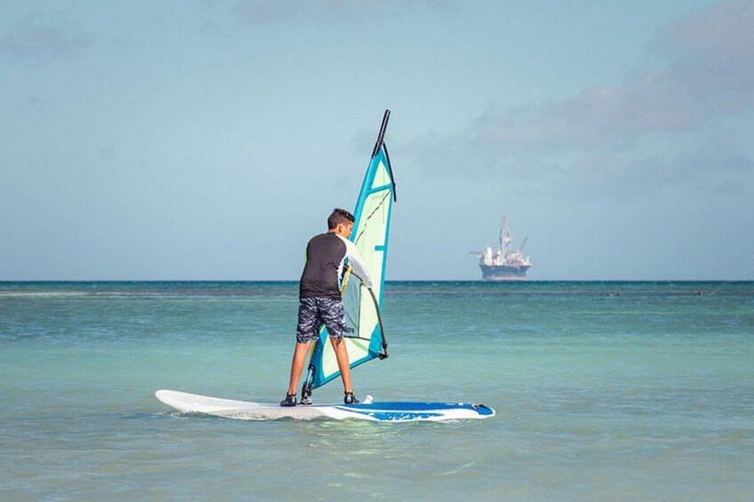 Une personne pratiquant la planche à voile par une journée ensoleillée, avec un navire en arrière-plan. 3