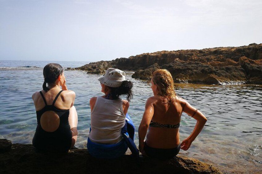 Three people sitting on rocks by a body of water with a rocky shoreline in the background. 3