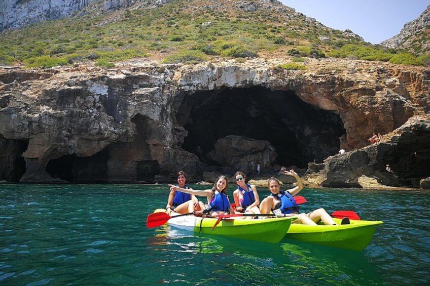 A group of people in a green kayak on clear water with a rocky cave in the background. 4