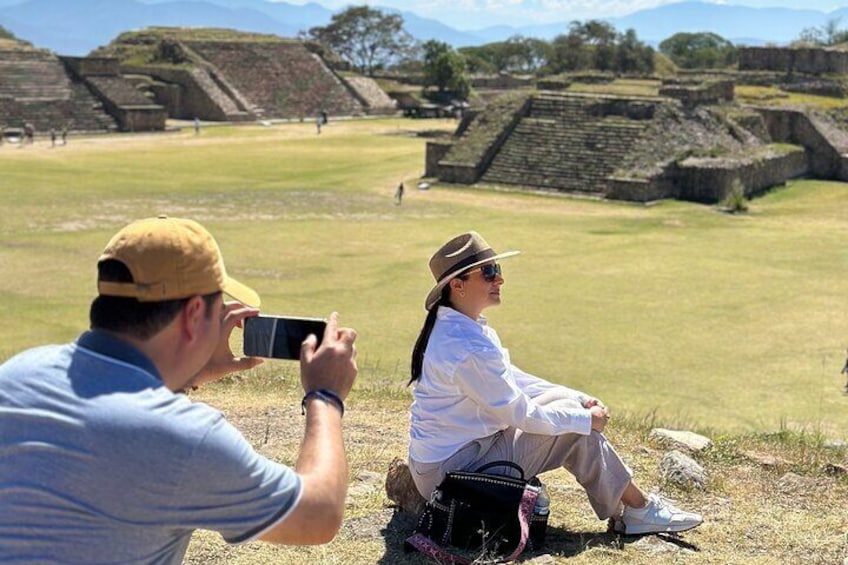 Two people sitting on the grass near ancient ruins with pyramids in the background. 1