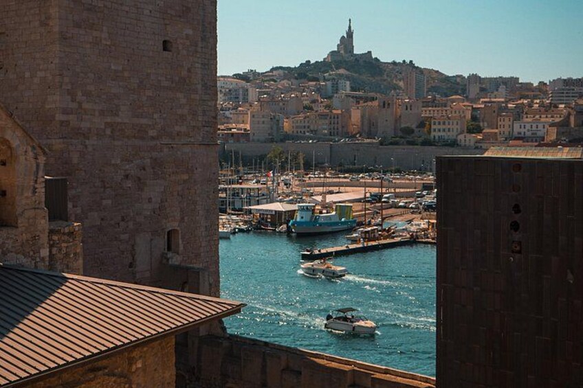 Eine Küstenstadt mit einem markanten Turm, einer Marina voller Boote und einem Hügel im Hintergrund mit einem Turm. 1