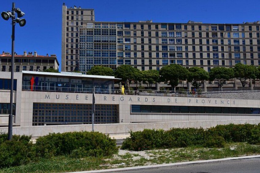 Das Gebäude des Musée Régards de Provence bei blauem Himmel und umgebender Bepflanzung. 2