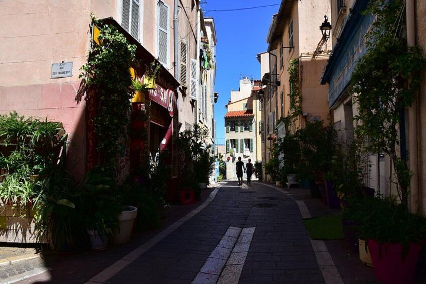 Eine enge Straße gesäumt von Gebäuden, Blumentöpfen und einem strahlend blauen Himmel. 3
