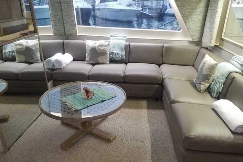 A cozy living room with a brown sofa, a round glass coffee table, and a view of boats through a large window. 2