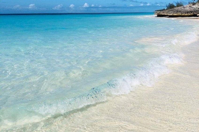 Una playa con agua turquesa cristalina, arena blanca y un promontorio rocoso a lo lejos. 2