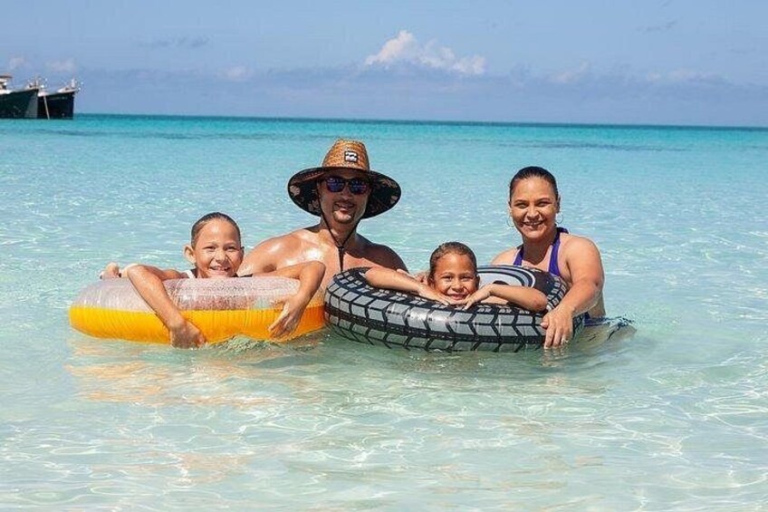 Una famiglia in un ambiente tropicale con acque turchesi cristalline, una barca sullo sfondo e cielo sereno. 2