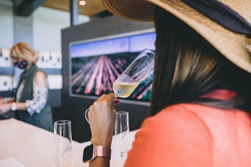 A person holding a wine glass, a table with glasses, and a screen displaying a racing track. 3