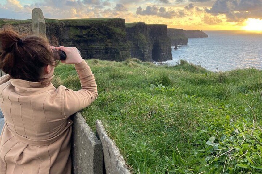 A person taking a photo of a coastal cliff with a sunset in the background. 4