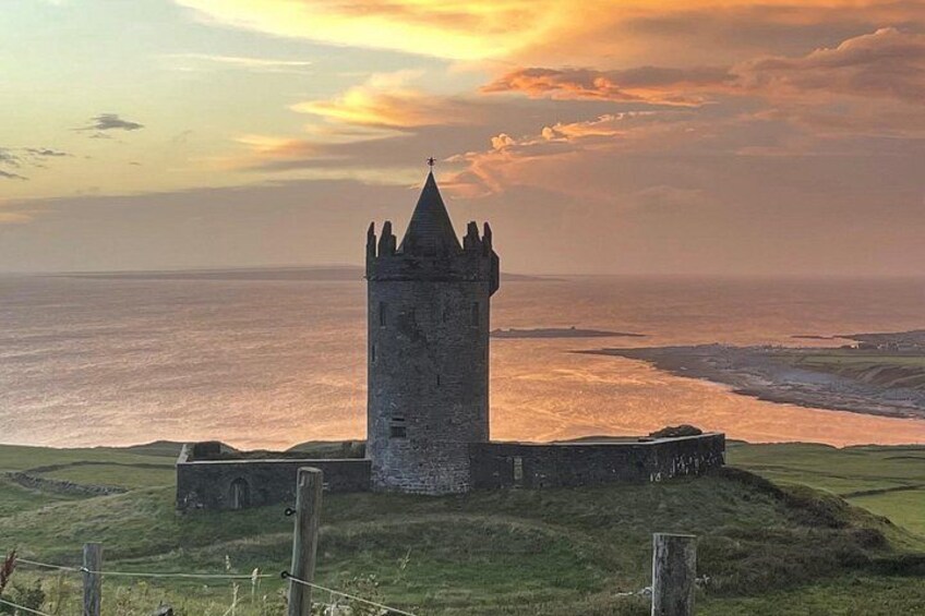 A tower with a pointed roof, surrounded by grassy terrain and a body of water in the background. 1