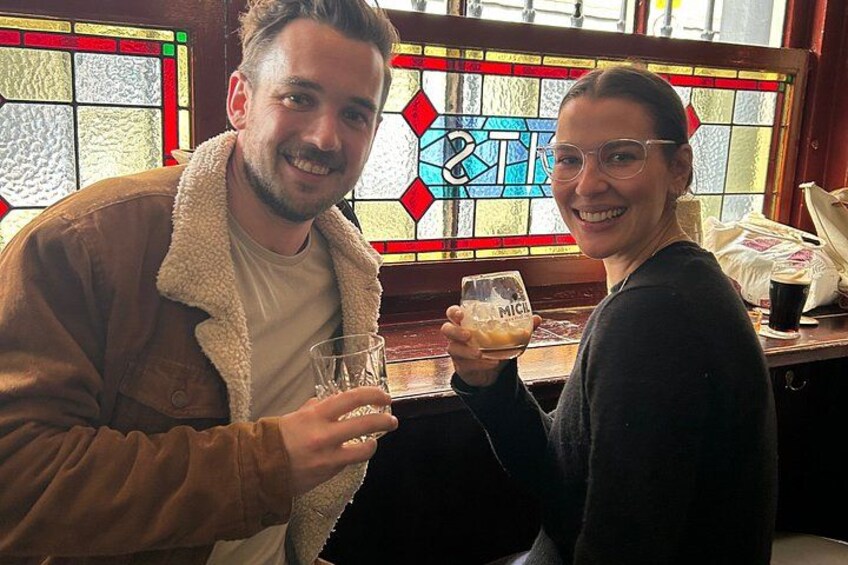 Two people sitting at a table in a bar with a stained glass window in the background. 2