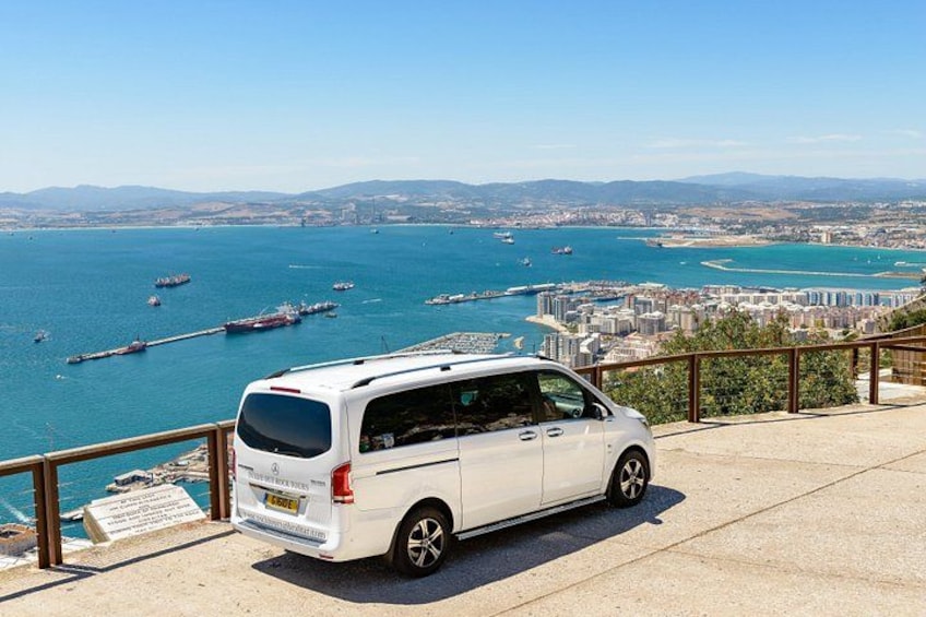 Un furgone bianco parcheggiato su una sporgenza in cemento con vista su una città costiera, un porto turistico ed edifici. 4
