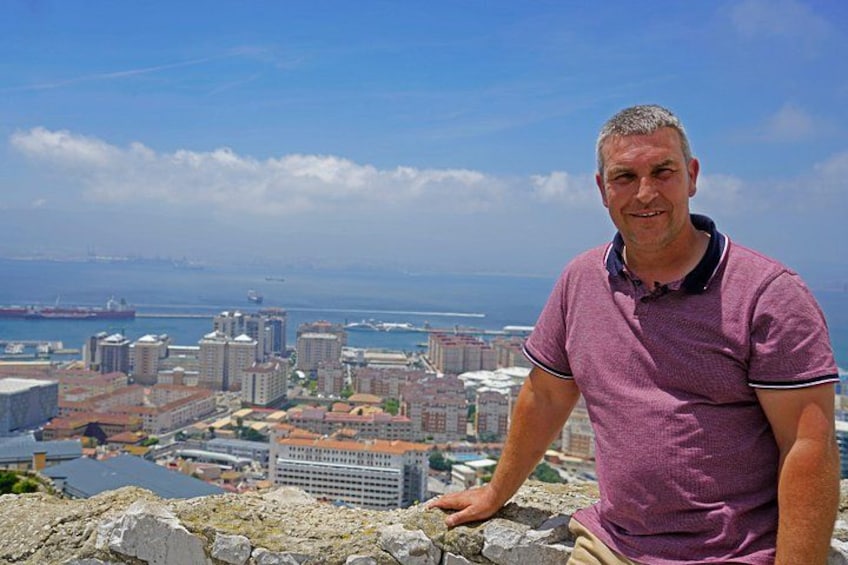 Un uomo in piedi su una sporgenza rocciosa, con vista su una città, edifici e un corpo d'acqua all'orizzonte. 2