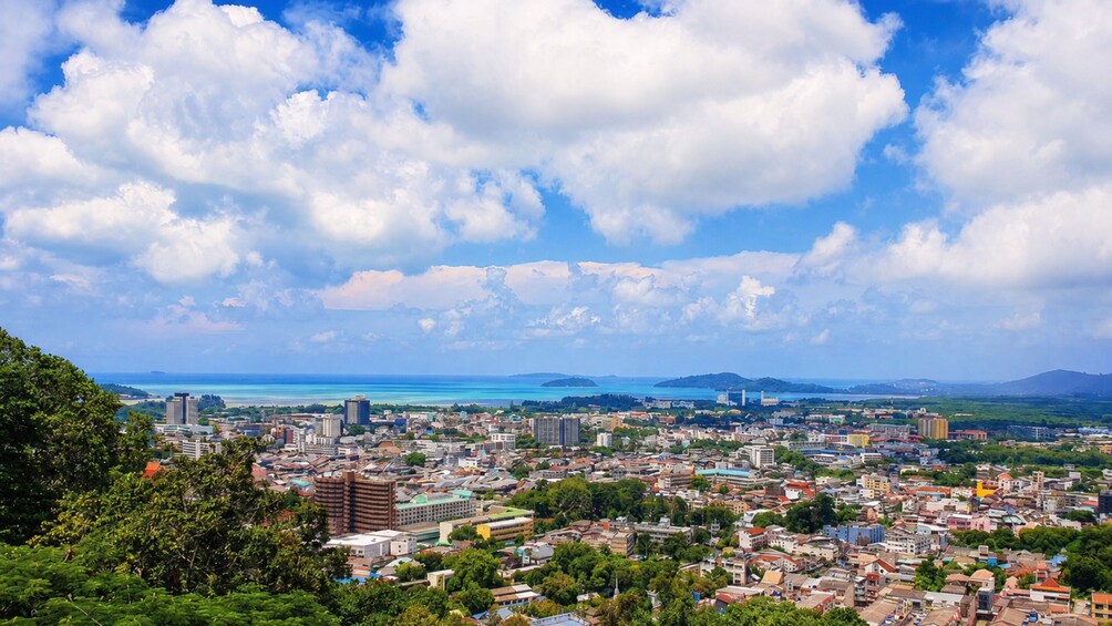 A coastal cityscape with dense urban buildings, a clear blue sky, and a distant view of the sea and islands. 5