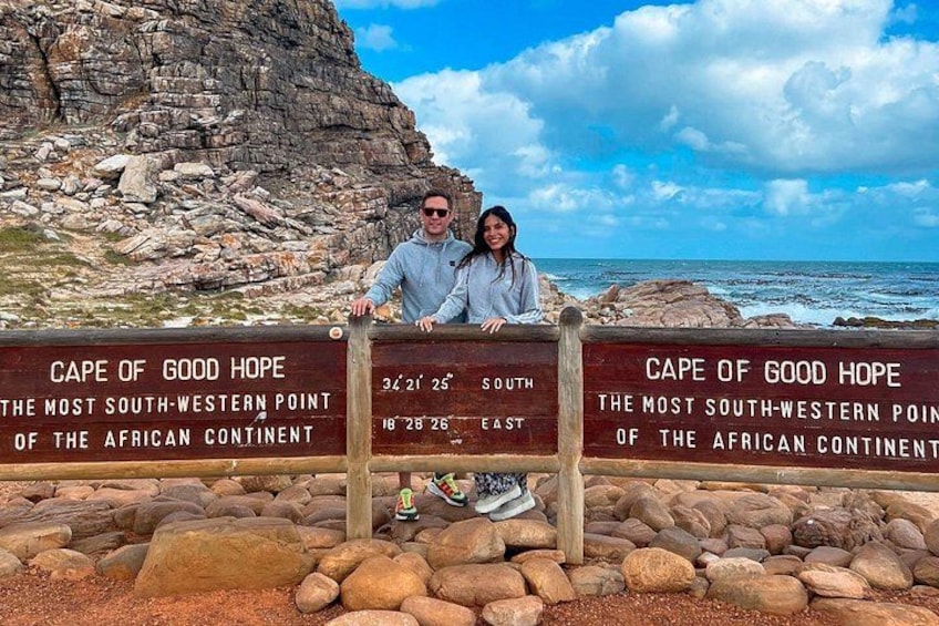 A couple at the Cape of Good Hope sign with the ocean and rocky terrain in the background. 2
