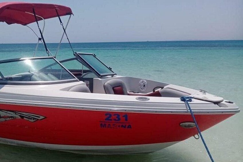 A red and white speedboat with the number 231 and the word 'MAGINA' on its side, docked at a beach with clear turquoise water. 2