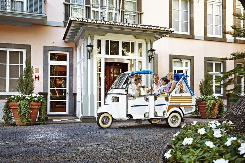 Un véhicule blanc à trois roues est garé devant un bâtiment sur lequel on peut lire l’inscription « H ». 1