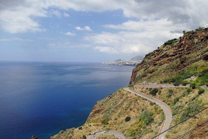 Une route côtière sinueuse offrant une vue sur l’océan et une ville située au loin. 2