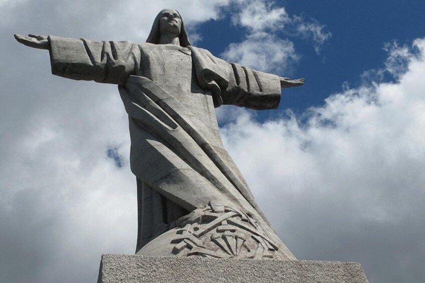 Una gran estatua de piedra con los brazos extendidos, sobre un cielo nublado. 5
