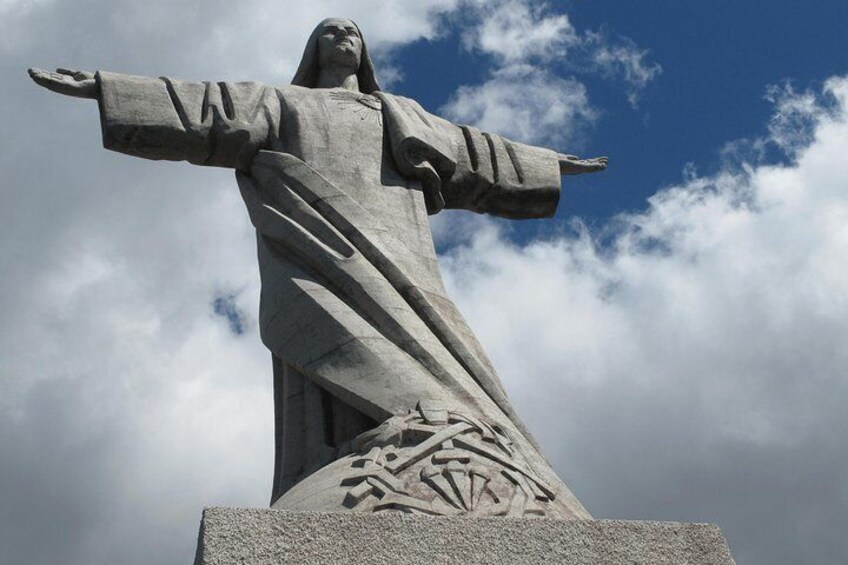 Une grande statue de pierre aux bras tendus, se détachant sur un ciel nuageux. 5