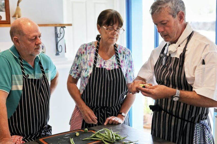 Three people wearing aprons, one cutting vegetables on a table. 1