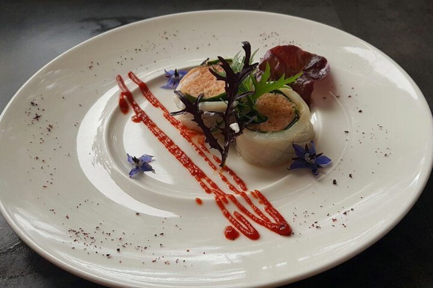 A white plate with a food item, garnished with red sauce and blue flowers. 3