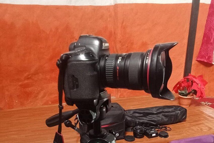A camera on a tripod with a lens, a bag, and some accessories on a wooden surface. 2