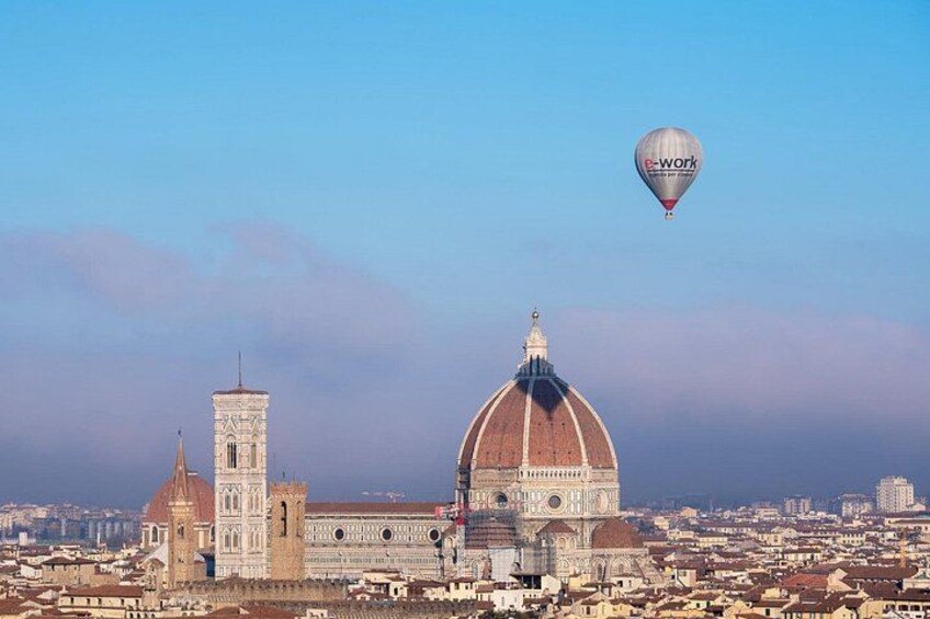 Eine Stadtansicht mit einer markanten Kuppel und einem Turm, ein Heißluftballon am Himmel, und ein klarer, blauer Himmel. 3