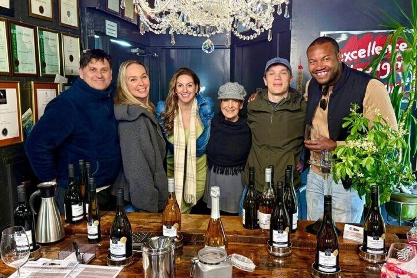 A group of people standing in front of a bar with various bottles of wine and glasses. 5