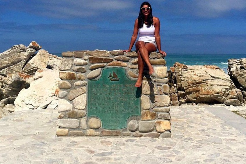 A woman sitting on a stone monument with a plaque, overlooking a rocky coastline and the ocean. 4