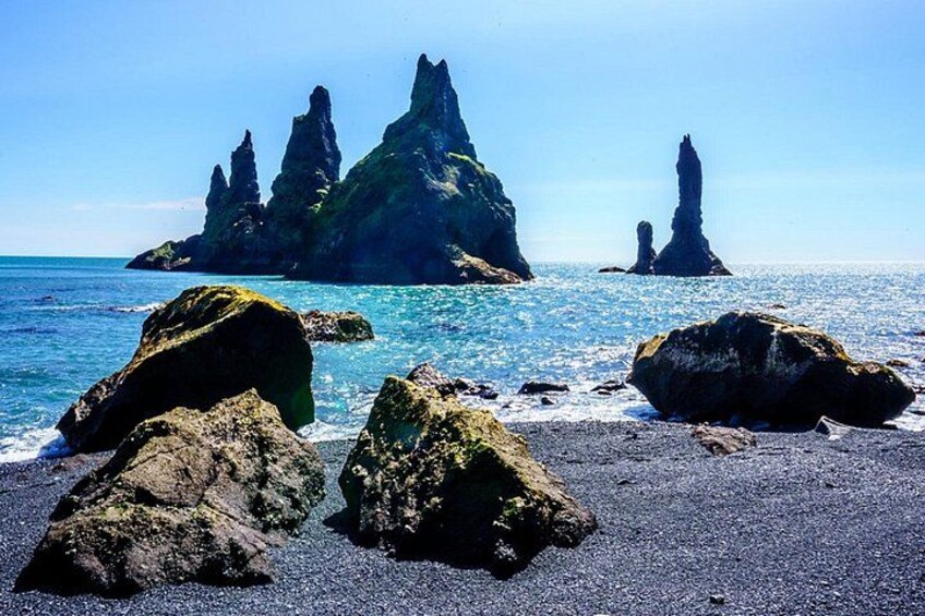 A rocky coastline with large boulders and tall, narrow rock formations in the background. 2