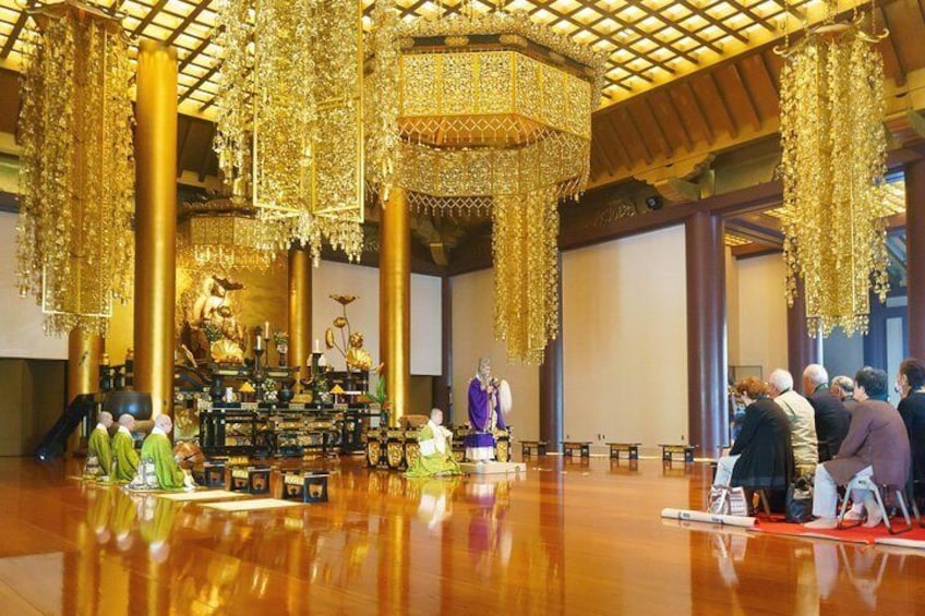 A grand hall with ornate golden chandeliers, a central altar, and attendees seated on the floor. 3