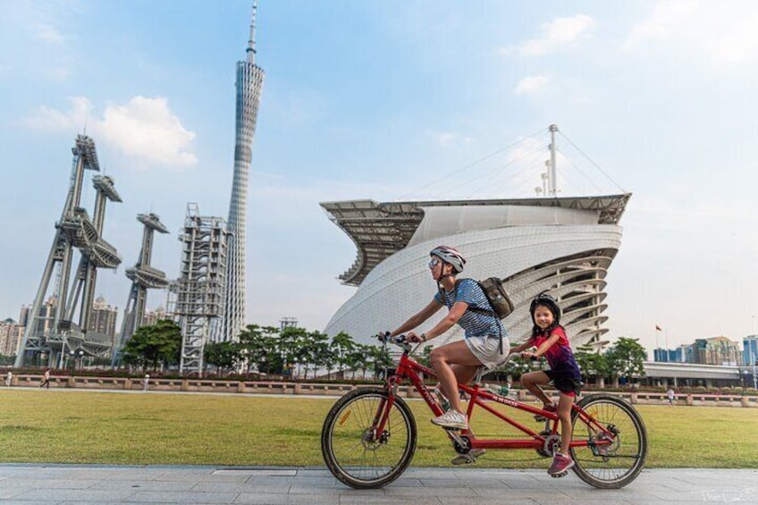 Two people riding bicycles in a park with modern architecture in the background. 5