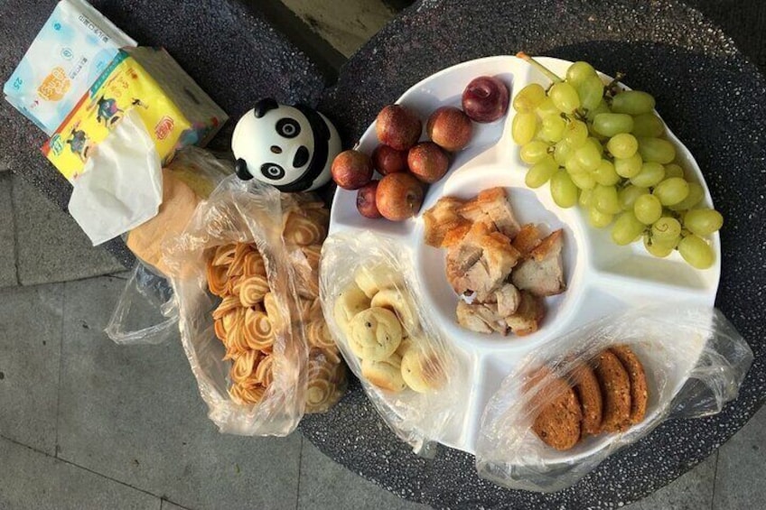 A picnic setup with various foods like grapes, peaches, cookies, and bread on a round table. 4