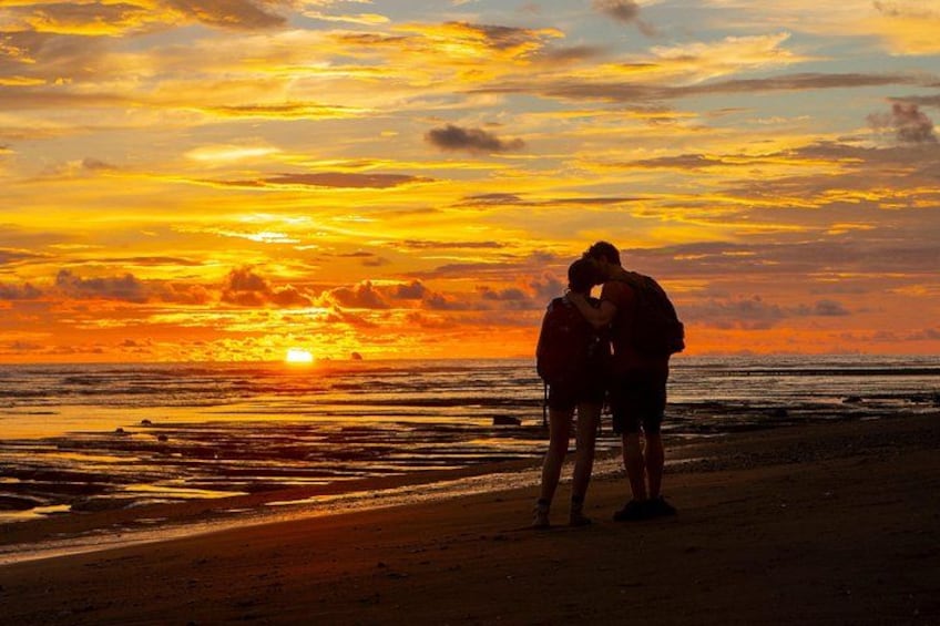 A sunset over a beach with two people embracing. 2