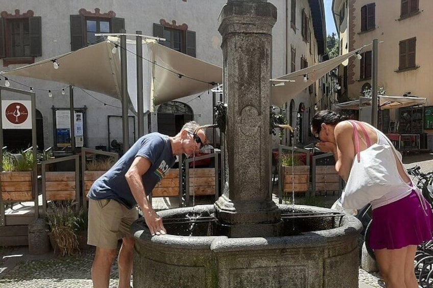 Due persone che interagiscono con una fontana in pietra in un ambiente esterno. 1